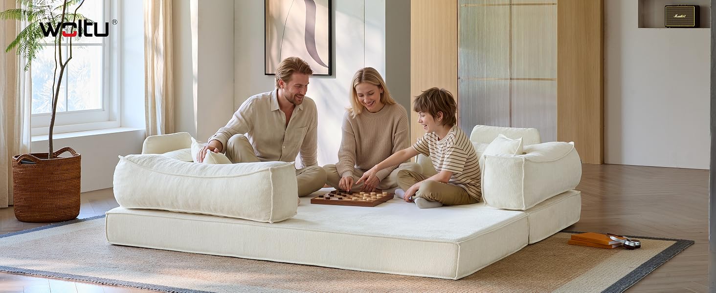 Tres personas sentadas juntas en un gran sofá seccional tapizado de color crema en una habitación moderna y luminosa con paredes blancas, ventanas y muebles de madera clara visibles en el fondo.