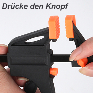 Gros plan d'une pince ou d'un mécanisme de poignée en plastique noir avec poignées oranges, montrant l'action d'une pression sur un bouton avec le texte allemand « Drücke