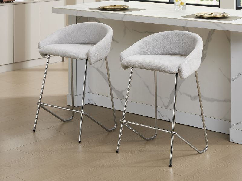 Deux tabourets de comptoir rembourrés modernes avec dossiers incurvés en tissu gris clair, dotés de bases et de repose-pieds en métal chromé.