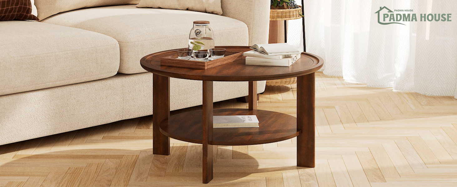 Round wooden coffee table with two tiers. Dark brown finish, placed in front of a beige sofa on hardwood flooring. Books and a glass on the tabletop.