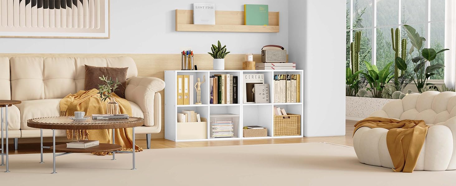 Modern living room with beige sofa, wooden coffee table, white shelving unit, and indoor plants. Bright, airy space with natural light.