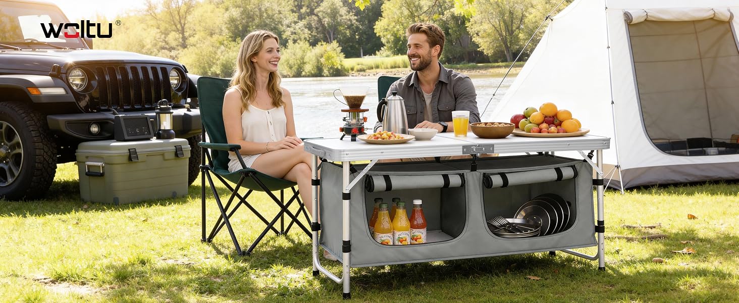 Text reads 'Watiti'.
[SENTENCE 14] Portable camping kitchen table setup outdoors with chairs, showing two people enjoying a meal near a vehicle.
[SENTENCE 15] Table features storage compartments below.