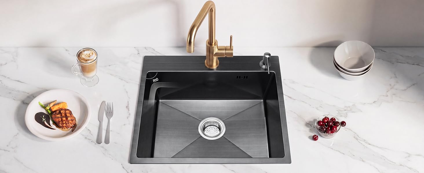 Vue aérienne d'un évier de cuisine en composite noir avec robinet unique, entouré de vaisselle blanche, d'ustensiles, de fruits secs et d'éléments décoratifs sur une surface claire.