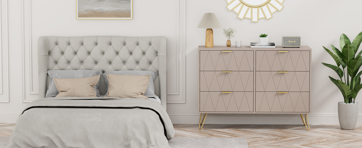 Intérieur de chambre moderne avec tête de lit grise capitonnée, commode beige, miroir décoratif et plante en pot. Esthétique épurée et minimaliste avec éclairage naturel.