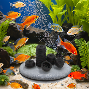 Aquarium scene with colorful fish swimming around a circular stone air diffuser. Bubbles rise from the diffuser, surrounded by green plants and a sandy bottom.