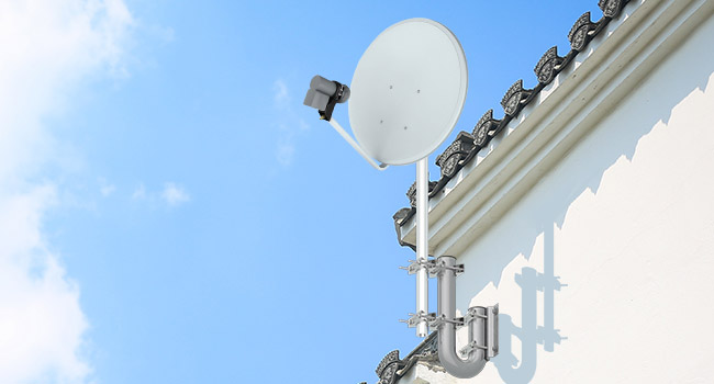 White satellite dish mounted on a building roof against a blue sky. Multiple antennas or receivers visible on the dish.