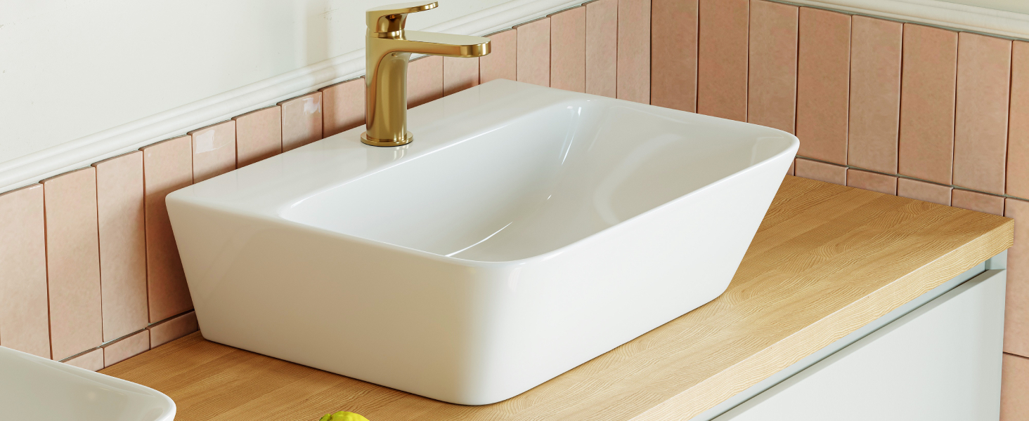 Lavello rettangolare in ceramica bianca su piano di lavoro in legno. Alzatina piastrellata rosa visibile dietro il lavandino
