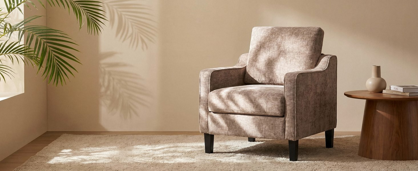 Beige upholstered armchair with rolled arms and wooden legs, positioned in minimalist interior space next to small side table and lamp.