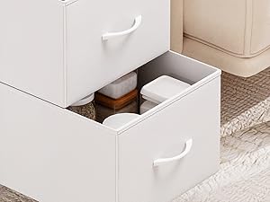Le tiroir de rangement blanc de la chambre à coucher s'ouvre, révélant des compartiments avec du linge de maison et des textiles pliés, présentés dans un décor de chambre minimaliste avec tapis et meubles.
