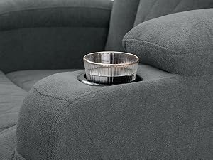 de vidrio transparente integrado en el reposabrazos del sofá de tela gris. Portavasos circular con borde metálico visible, diseñado para sostener bebidas de forma segura mientras está sentado
