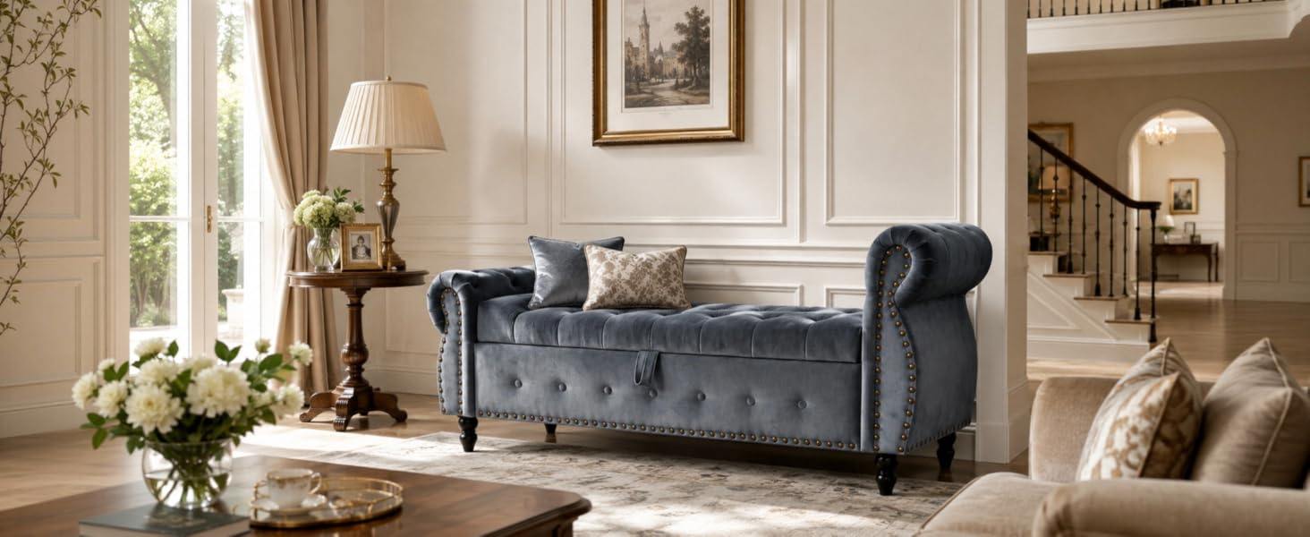 Dark blue upholstered Chesterfield-style sofa with rolled arms and tufted back, positioned in elegant living room with table lamps and floral arrangement.