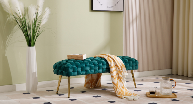 Teal tufted bench with gold legs in a living room setting. White vase with pampas grass, throw blanket, and decorative tray on tiled floor nearby.