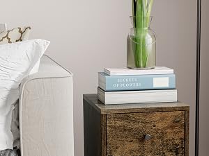Rustic wooden bedside table with mirrored surface. Placed in bedroom next to white bed, with decorative items on top and patterned rug below.