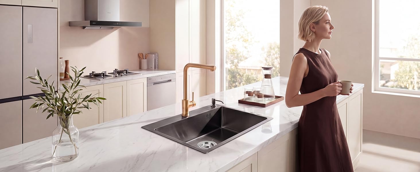 Femme en robe bordeaux utilisant une cuisinière à gaz noire dans une cuisine moderne et lumineuse avec des armoires blanches et de grandes fenêtres.