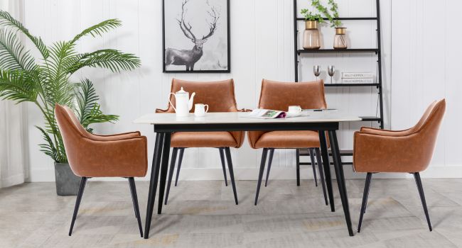 avec table rectangulaire blanche, quatre chaises en cuir beige avec de fins pieds noirs. Étagère en échelle noire et illustration de cerf en arrière-plan. Palmier en pot pour la décoration.