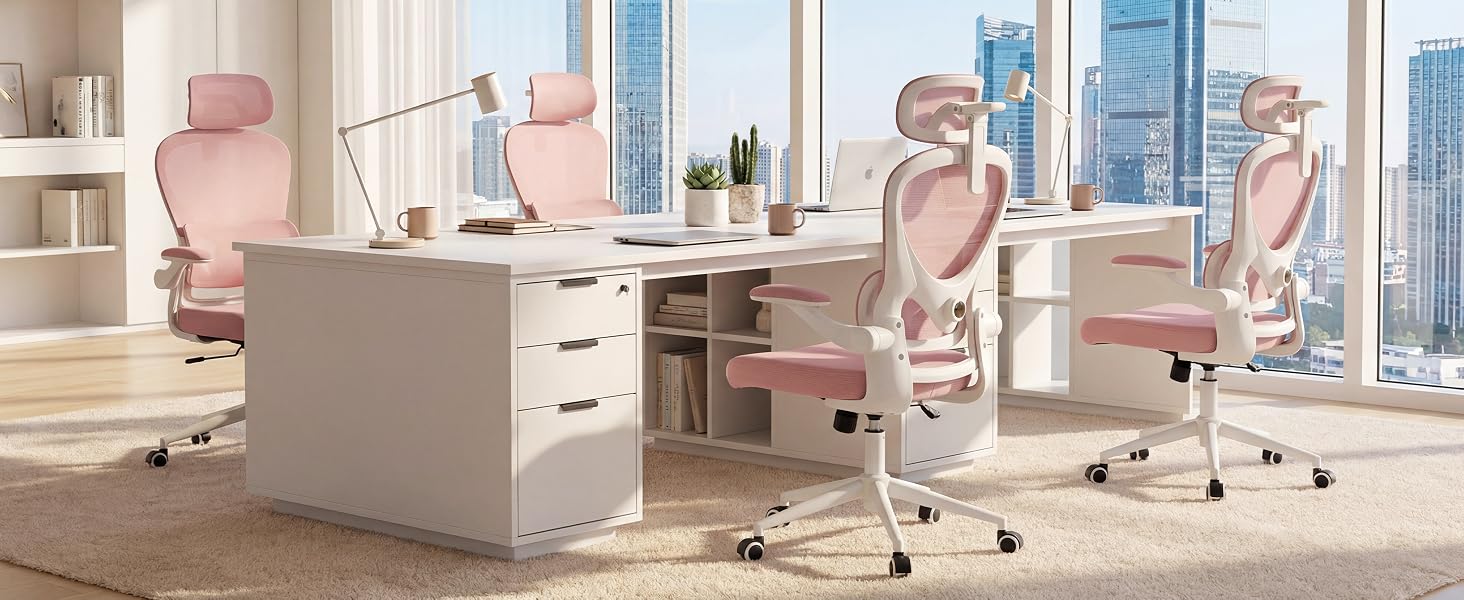 Modern office workspace with minimalist aesthetic featuring light wood desk, white storage unit, pink office chair, and city skyline view through floor-to-ceiling windows. Multiple workstations visible in collaborative environment.