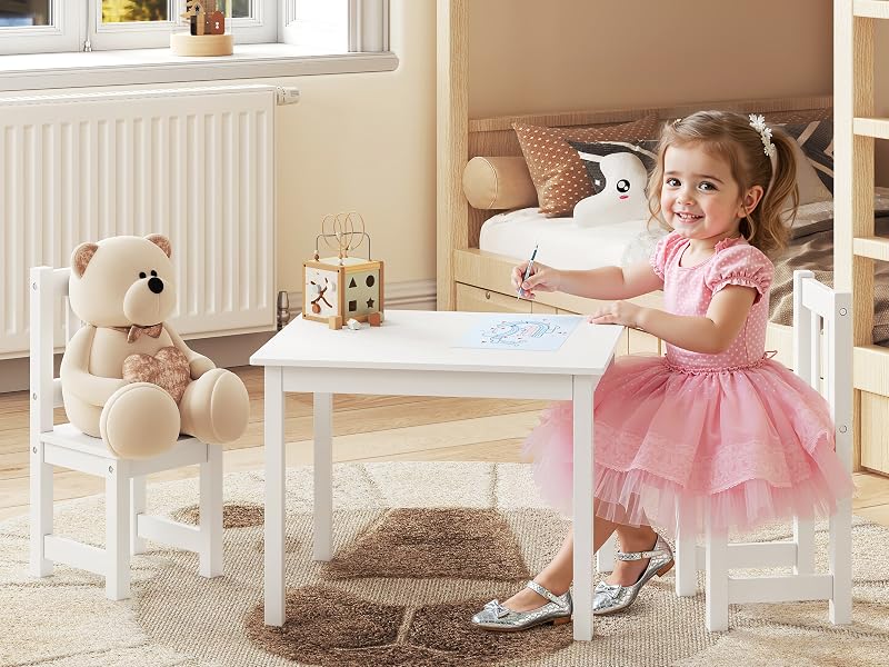 Sala giochi per bambini con tavolo e sedie in legno bianco, allestito con orsacchiotti e giocattoli.