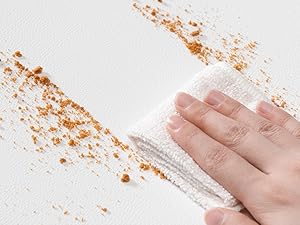 Pulire a mano la polvere o i detriti arancioni da una superficie di colore chiaro, dimostrando l'azione di pulizia o manutenzione.