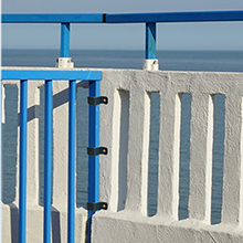 White stucco wall with bright blue gates or railings along what appears to be a seaside or waterfront location.
