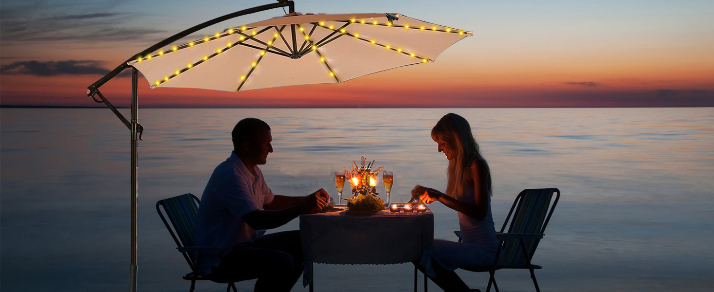 Outdoor dining setup at sunset with illuminated patio umbrella featuring LED lights along its ribs, overlooking calm water horizon.