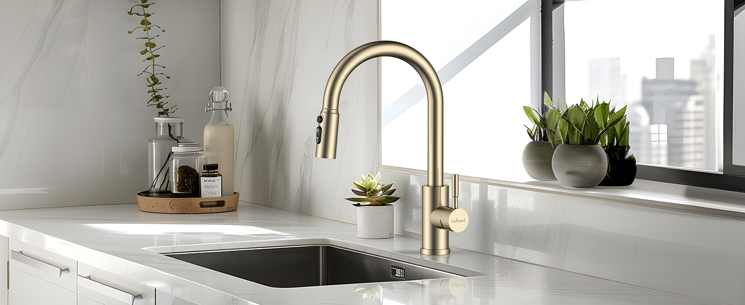Modern brushed gold kitchen faucet with pull-down sprayer, installed in white countertop with stainless steel sink near window.