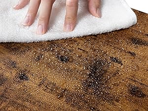 Primo piano della mano che pulisce una superficie di legno con un panno bianco, rivelando