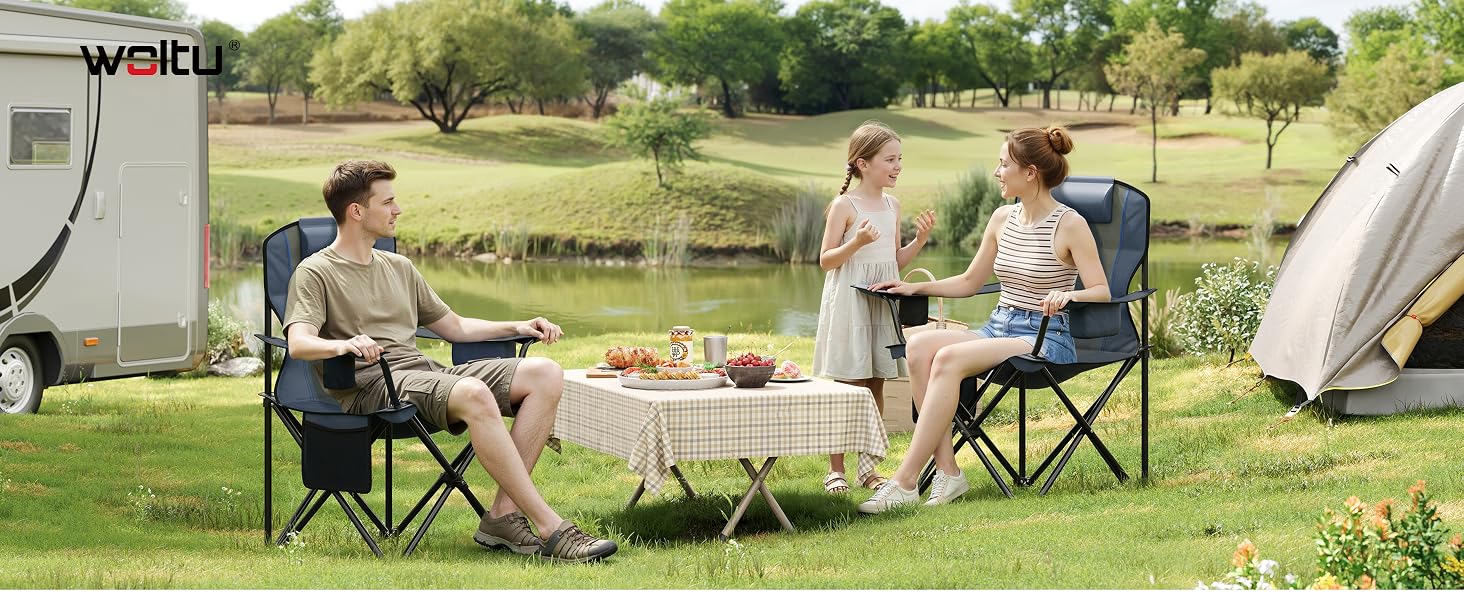 Escena de campamento al aire libre con personas sentadas en sillas portátiles alrededor de una mesa plegable, con RV y carpa de fondo. Entorno de césped natural con árboles.