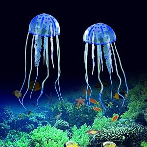 Two glowing blue jellyfish-shaped aquarium decorations floating above colorful coral reef in dark water.