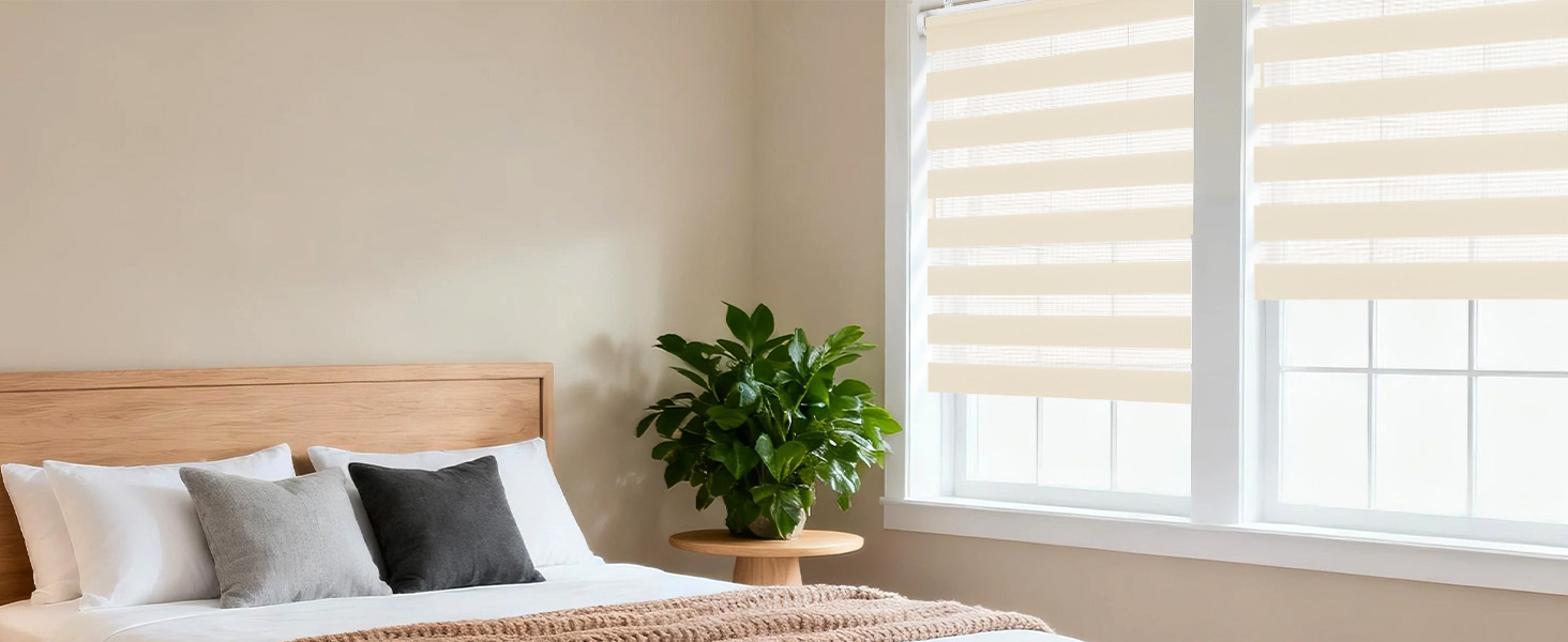 L'intérieur de la chambre moderne comprend des stores zébrés et doubles sur les fenêtres, laissant filtrer la lumière naturelle. Palette de couleurs neutres avec murs et literie blancs.