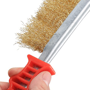 A hand holding a wire brush with a red plastic handle and metal bristles, used for cleaning or scrubbing surfaces.