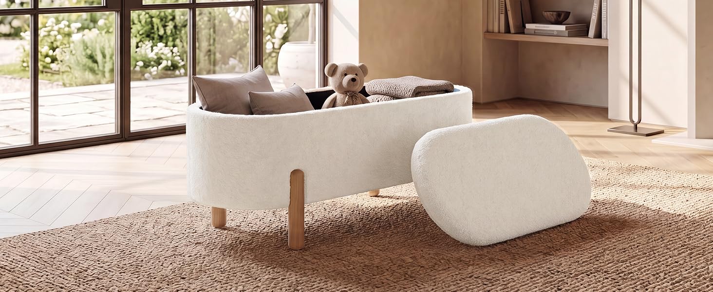 Modernes Wohnzimmer mit cremefarbener runder Ottomane, beigem Polstersofa, Holzregalen, großen Fenstern und Teppich aus Naturfasern auf hellem Boden.