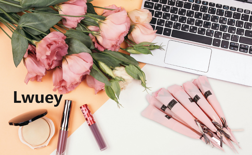 Flatlay of makeup products on desk with keyboard and pink roses. Includes foundation, lipstick, makeup brushes, and other cosmetic items, showcasing beauty and technology blend.