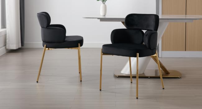 Dos sillas de comedor modernas con tapicería negra y patas de metal en tono dorado, colocadas cerca de una pequeña mesa redonda contra un piso de madera clara