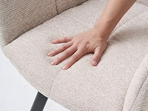 Gros plan de la main posée sur un tissu beige texturé, démontrant la texture douce et tissée de la surface des meubles rembourrés.