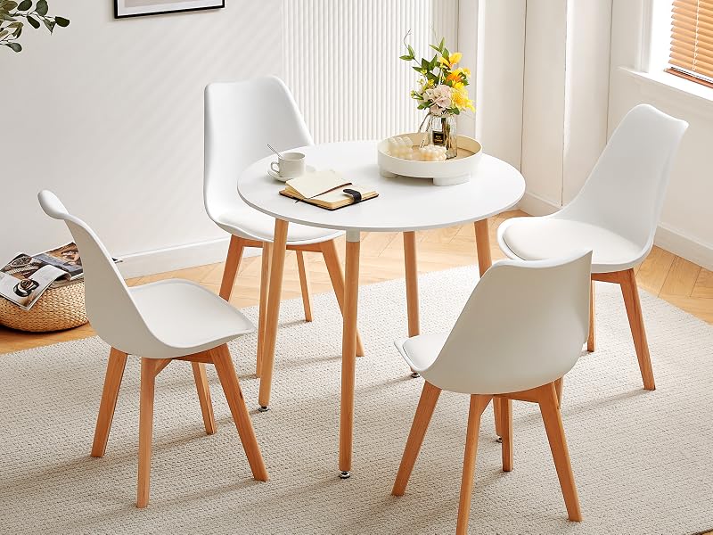 avec table ronde blanche et quatre chaises blanches avec pieds en bois, placé dans une pièce lumineuse avec rideaux et décoration murale.