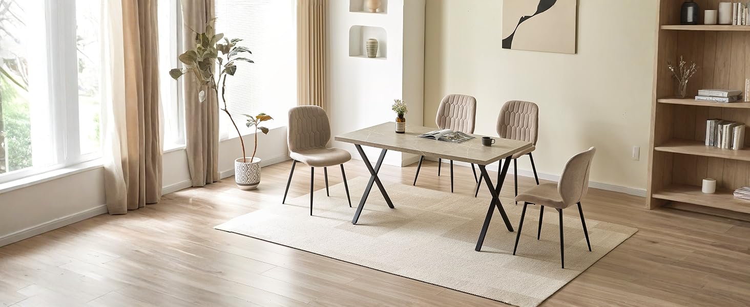 L'intérieur de la salle à manger minimaliste comprend une table ronde blanche avec quatre chaises grises modernes, de grandes fenêtres avec des rideaux neutres, du parquet et des étagères en arrière-plan.