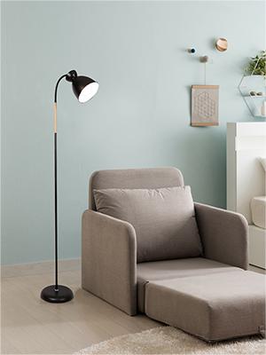 Beiger Sessel mit ausziehbarer Fußstütze, begleitet von einer schwarzen Stehlampe mit Holzakzent. Vor einer hellblauen Wand in einer minimalistischen Raumumgebung