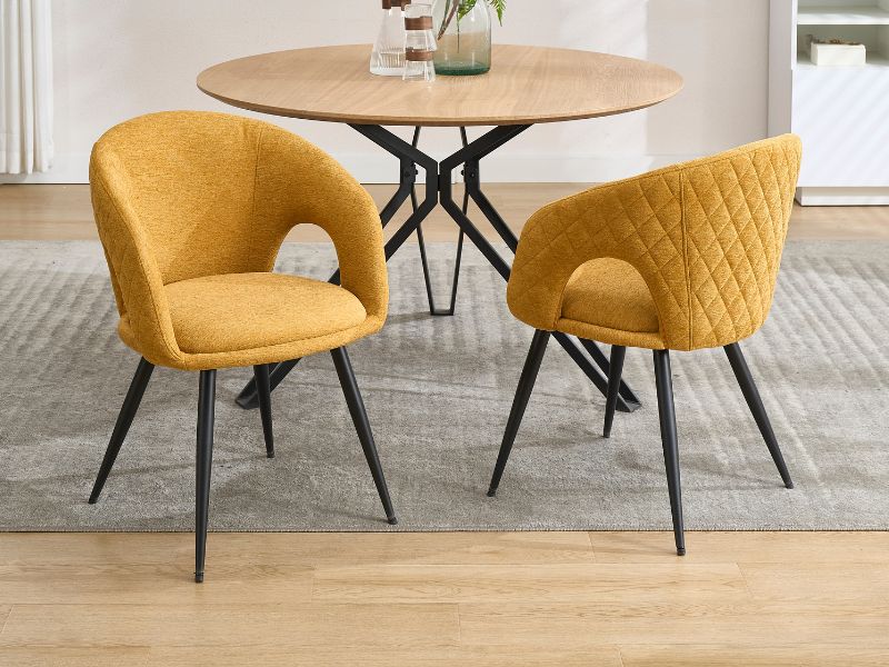 Ensemble de salle à manger moderne comprenant une table ronde en bois avec base en métal noir et deux chaises d'appoint matelassées jaune moutarde à dossier incurvé.