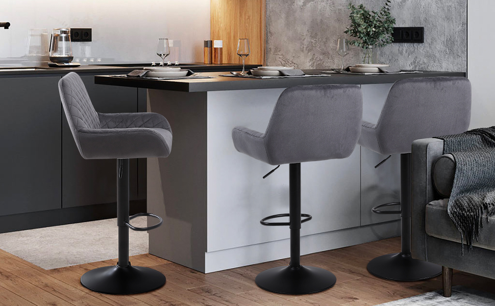 Two gray velvet bar stools with cushioned seats and backrests, positioned at a dark kitchen counter against white cabinets.