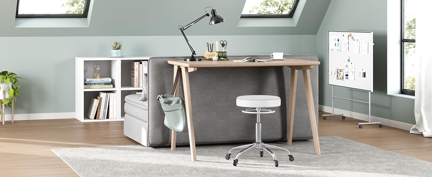 Moderna configuración de oficina en casa con escritorio de madera, unidades de almacenamiento blancas, lámpara de escritorio ajustable y silla con ruedas blanca en una habitación con paredes de color verde salvia.