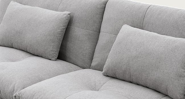 Detalle detallado de un sofá o seccional tapizado en gris que muestra cojines de felpa, una superficie de asiento con mechones y una textura de tela suave con un color gris neutro.