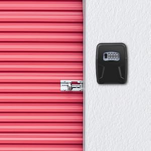 Wall-mounted key safe box with digital combination lock, displayed next to a red metal roll-up door, suggesting storage facility security use.