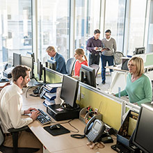 Espace de bureau moderne avec des personnes travaillant à des bureaux. Espace ouvert et lumineux avec de grandes fenêtres, des ordinateurs et des employés effectuant diverses tâches.