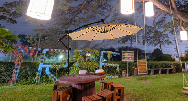 Outdoor dining area with wooden picnic table, illuminated patio umbrella, and hanging lights. Garden setting at dusk.