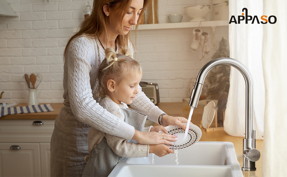 a woman and a little girl washing hands in a kitchen sink.