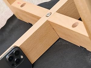 Support ou support de téléphone en bois avec fente noire, photographié en angle sur une surface sombre avec le smartphone visible sur le bord.