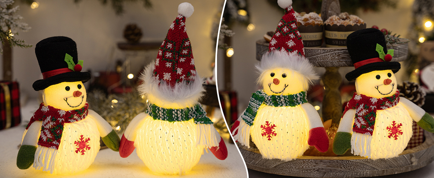 Vier beleuchtete Schneemanndekorationen mit Häten und Schals, angeordnet auf einer Oberfläche mit verschwommenen Weihnachtslichtern im Hintergrund
