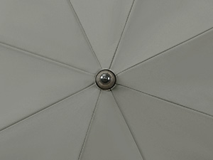 Close-up of a circular light fixture or ceiling vent with metal spokes radiating from a central point against a white surface.