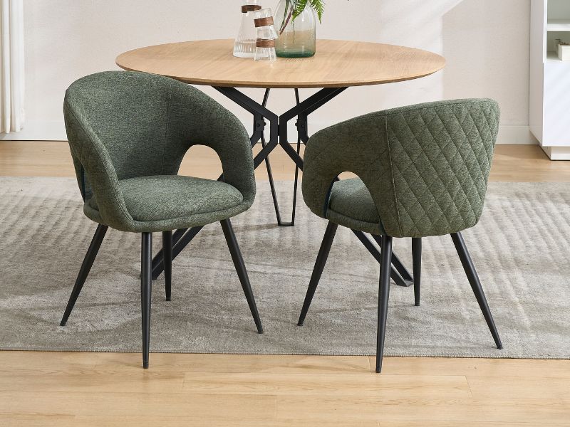 Table à manger ronde en bois avec base en métal noir, associée à deux chaises d'appoint matelassées vert sauge à dossier incurvé.
