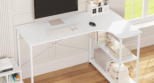 blanco en forma de L con estantería. Las características incluyen soporte para monitor, bandeja para teclado y estantes de almacenamiento laterales. Ubicado en una habitación luminosa con ventana.